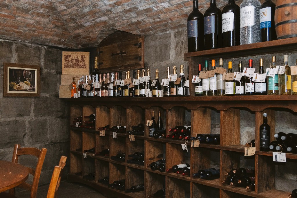 Adega privativa da Trattoria Primo Camilo, com garrafas nas prateleiras de pedra