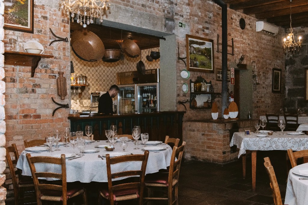 Sala superior da Trattoria Primo Camilo, com mesa posta e lustres de cristal