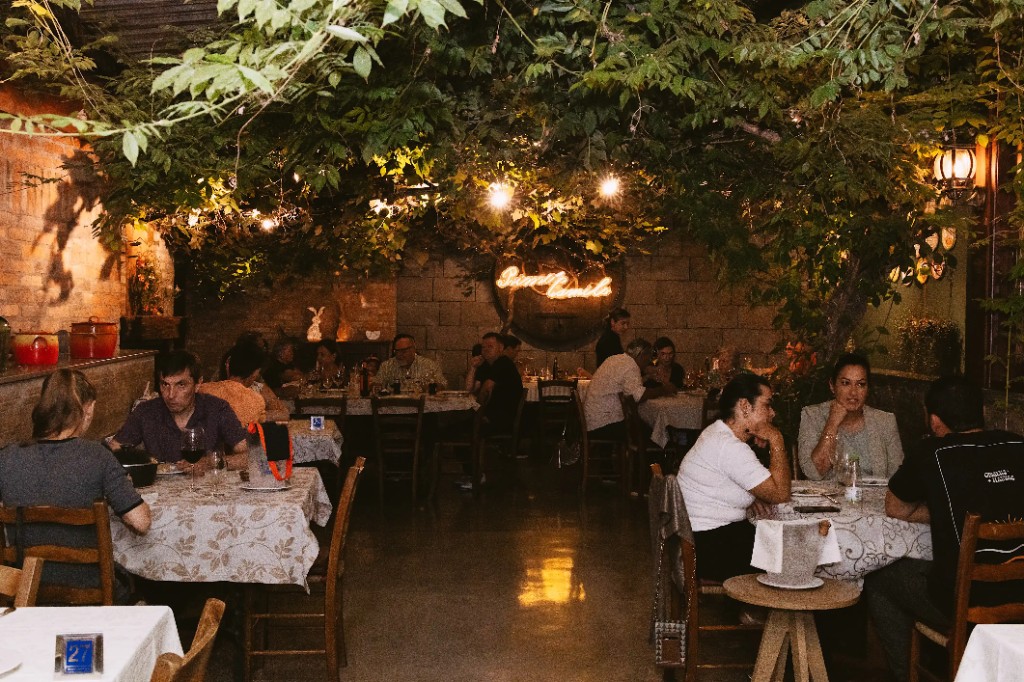 Salão principal da Trattoria Primo Camilo, com parreiral e mesas postas