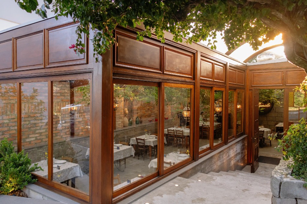 Varanda envidraçada da Trattoria Primo Camilo, com mesas postas e luz quente